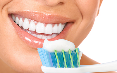 Toothbrush with toothpaste on it with a nice smile in the background